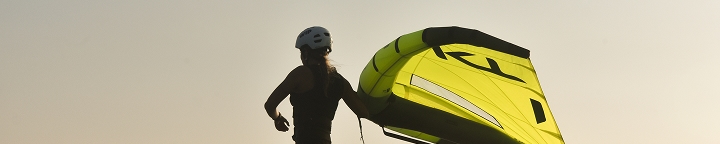 Praticante de wingfoil segurando a asa amarela em silhueta