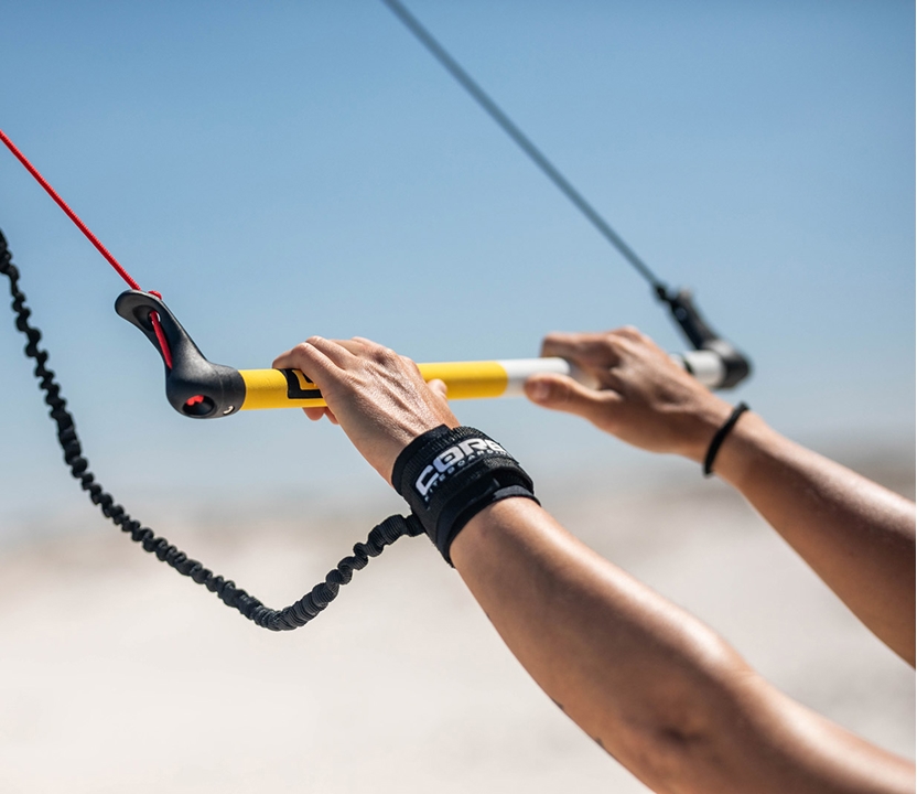 Mãos segurando a barra de controle do kite, com pulseira de segurança da Core